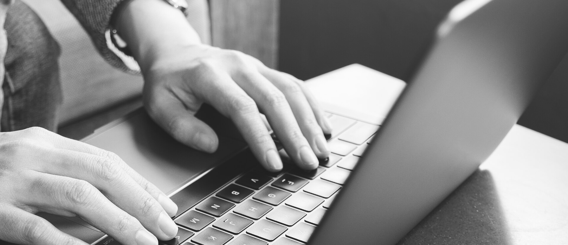 Close up of man's hands typing on a laptop, in black and white